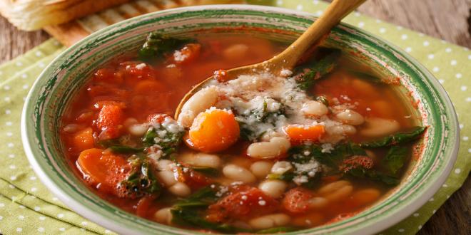 a bowl of tomato-based soup with beans and spinach